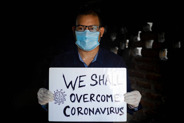 Młody człowiek w masce medycznej i rękawiczkach ochronnych stoi z tabliczką z wiadomością do "Pokonamy Coronawirusa". Mężczyzna z tabliczką Masaż. - Zdjęcie, obraz