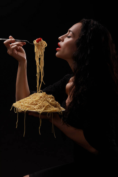 Een mooi meisje eet met een vork spaghetti met rode lippen. - Foto, afbeelding