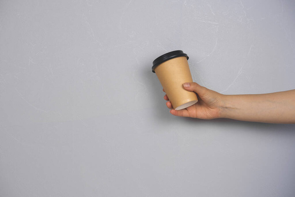 female hand holding coffee to go blank cup against concrete gray wall copy space - Photo, image