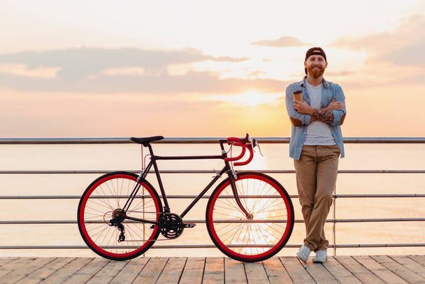 young bearded man traveling on bicycle at sunset sea - Foto, Imagen