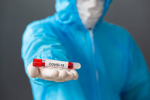 Medische wetenschapper die PBM draagt en bloed vasthoudt van geïnfecteerde persoon covid-19 voor vaccinonderzoek voorkomt of behandelt het nieuwe coronavirus SARS-CoV-2, arts-wetenschapper of onderzoeksdoktersconcept - Foto, afbeelding