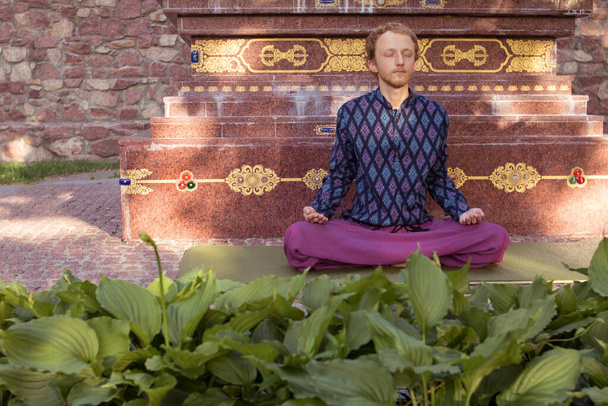 Buddhist man in a purple shirt meditates on the background of a Buddhist statue - Фото, зображення