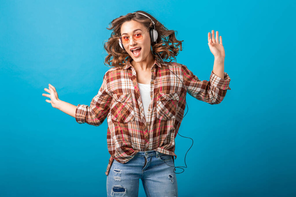 attractive smiling emotional woman jumping with funny crazy face expression in checkered shirt and jeans isolated on blue studio background, wearing pink sunglasses - Photo, Image