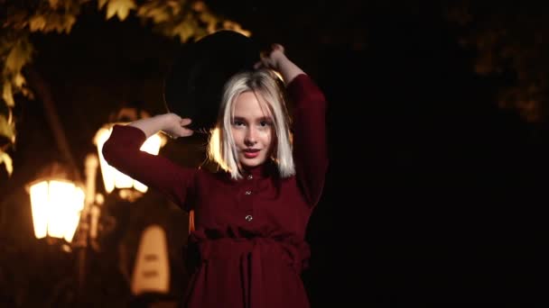 Millennial hipster woman with blond hairstyle dancing under the lantern of city street at night. Hat, nose piercing. Funny girl. Slow motion. - Video