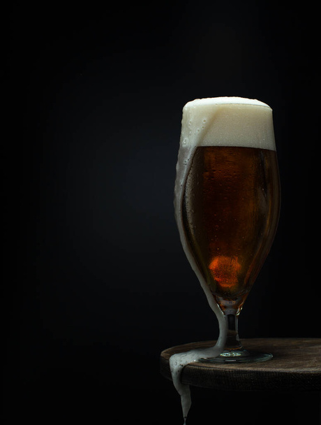 Glass of cold fresh beer with leaky foam on wooden table on black background.Close up. - Fotografie, Obrázek