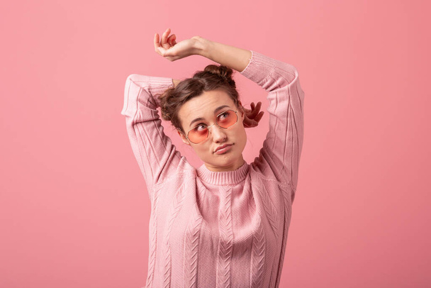 young pretty thinking dreaming woman in stylish spring outfit wearing pink sweater and sunglasses isolated on pink studio background, looking up - 写真・画像