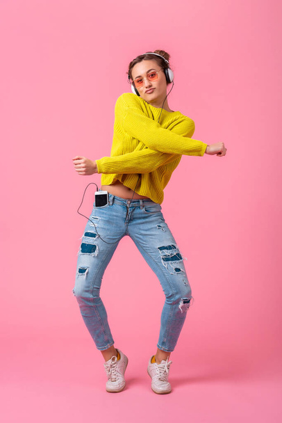 attractive happy funny woman in yellow sweater jumping listening to music in headphones dressed in hipster colorful style outfit isolated on pink studio background, having fun - Foto, afbeelding