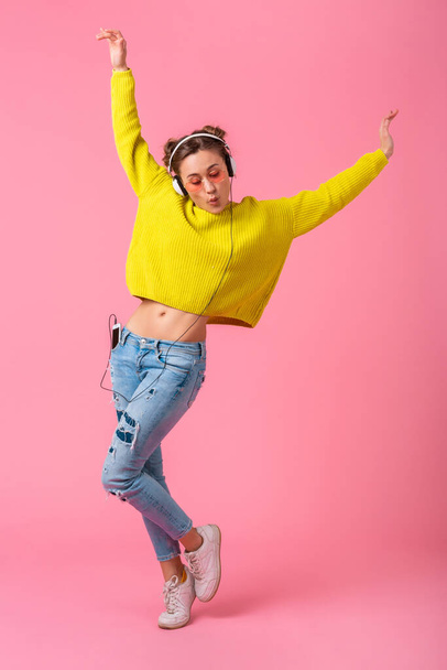 attractive happy funny woman dancing listening to music in headphones dressed in hipster colorful style outfit isolated on pink studio background, wearing yellow sweater and sunglasses, having fun - Foto, Bild