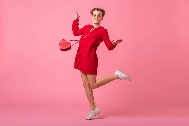 attractive happy smiling stylish woman in red trendy dress jumping running on pink studio background isolated, spring summer fashion trend, romantic mood flirty girl - Fotoğraf, Görsel