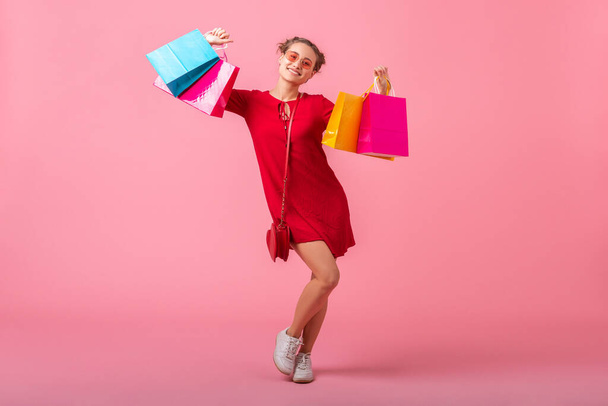 attractive happy smiling stylish woman shopaholic in red trendy dress holding colorful shopping bags on pink studio background isolated, sale excited, spring summer fashion trend - Foto, imagen