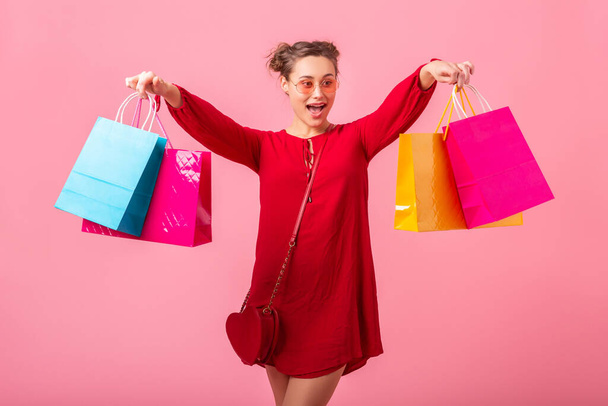 attractive happy funny emotion stylish woman shopaholic in red trendy dress holding colorful shopping bags on pink studio background isolated, sale excited, spring summer fashion trend - Fotó, kép