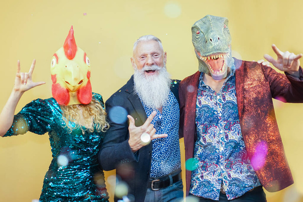 Lidé tančí na karnevalové párty v T-rexu a kuřecí masce. Přátelé baví poslech rockové hudby - Funny trend koncept - Obrázek - Fotografie, Obrázek