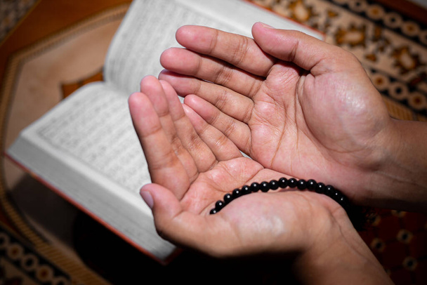 Jovem muçulmana rezando com Tasbeeh. O Alcorão Sagrado é o pano de fundo, Interior. Foco nas mãos
. - Foto, Imagem