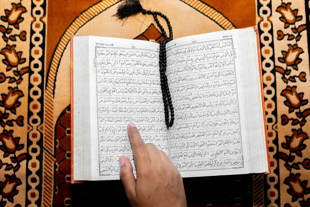 Mulher muçulmana lendo o Alcorão Sagrado usando o dedo. O Alcorão Sagrado no tapete de orações. Vista de ângulo superior. Interior
. - Foto, Imagem