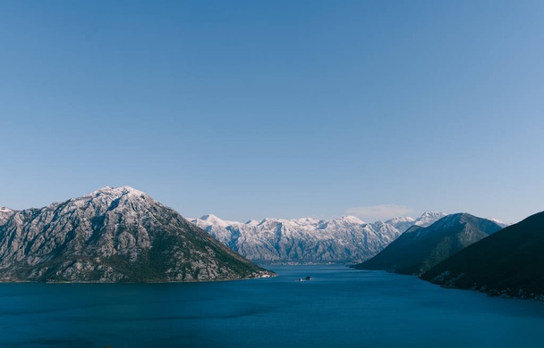 Панорамный вид с горы в заливе Кото в Черногории, в районе Пераст и Рисан. Заснеженные горные вершины зимой и голубая морская вода залива
. - Фото, изображение