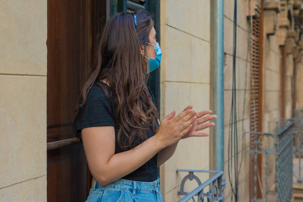 Hiszpańska młoda dziewczyna bije brawo z balkonu swojego mieszkania na rzecz hiszpańskiej służby zdrowia przeciwko Covidowi 19 - Zdjęcie, obraz