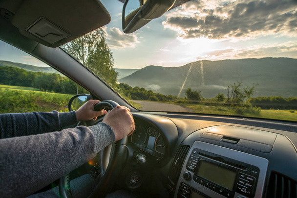Ταξιδεύοντας με το αυτοκίνητο σε ένα ορεινό δρόμο άνθρωπος κρατώντας το τιμόνι φόντο ήλιο δέντρο καλό καιρό. Μεταφορά εμπορευμάτων. - Φωτογραφία, εικόνα