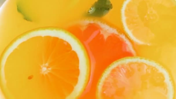 Vista desde la parte superior del tarro de limonada con naranjas flotantes, pomelos y hojas de menta fresca
 - Metraje, vídeo