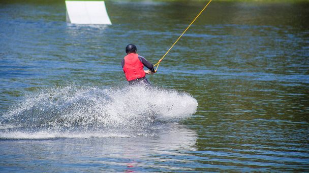 El hombre hace wakeboarding en el agua en el verano en un casco y traje de neopreno
. - Foto, Imagen