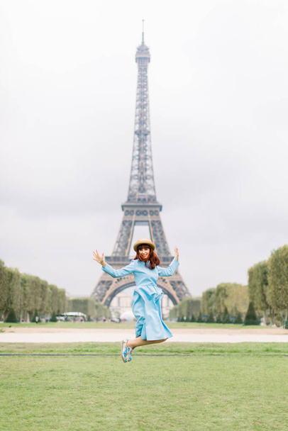 Paris girl at Eiffel Tower. Jumping happy smiling excited red haired girl in blue dress, having fun during vacations holidays in Paris, France, Europe - Photo, Image