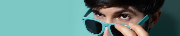 Крупный план молодого парня снимающего солнцезащитные очки на фоне акваменского цвета с копировальным пространством. Панорамный вид на баннер
. - Фото, изображение