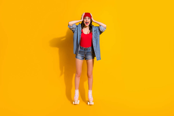 New roller skates sales omg. Full length photo excited surprised youngster fit girl rider impressed touch hands red headwear wear tank-top jeans isolated bright color background - Foto, Bild