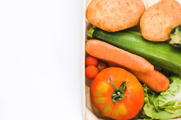 zelenina a zelenina uvnitř dřevěné krabice. Rajčata, mrkev, cuketa a salát. Bílé pozadí. Mezera pro text - Fotografie, Obrázek