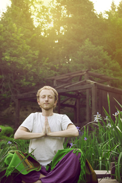 Red-haired male Buddhist meditates on a background of nature and old wooden house - Fotoğraf, Görsel