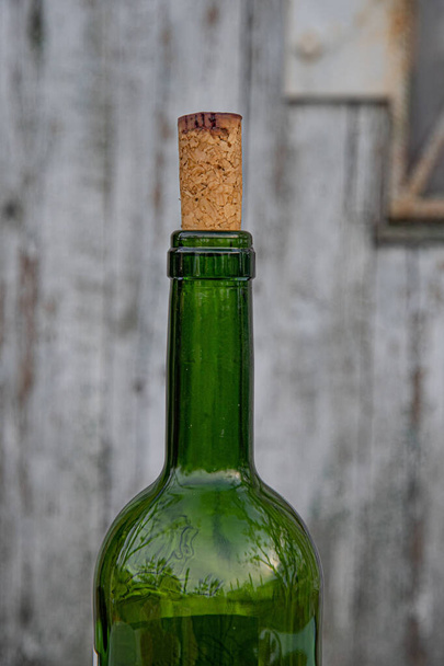Vista lateral del cuello de botella de vino cerrado con tapón de corcho texturizado natural manchado por vino tinto oscuro. Botella de vidrio verde primer plano sobre fondo de madera rústico borroso con espacio de copia
 - Foto, Imagen