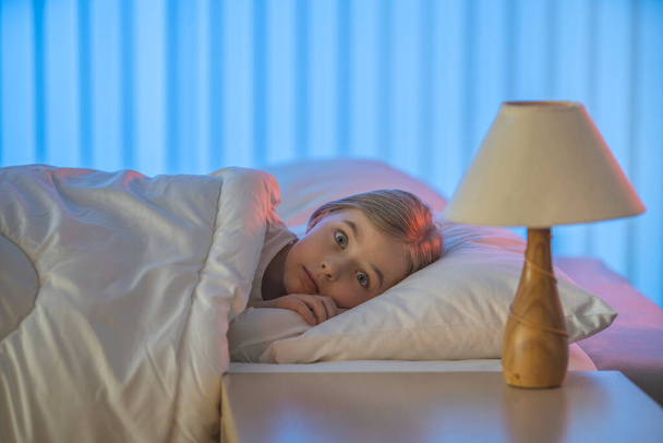The frightened girl lay on the bed. Evening night time - Φωτογραφία, εικόνα