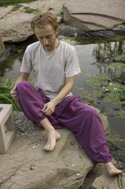 Joven pelirrojo sentado en una piedra cerca del lago
 - Foto, imagen