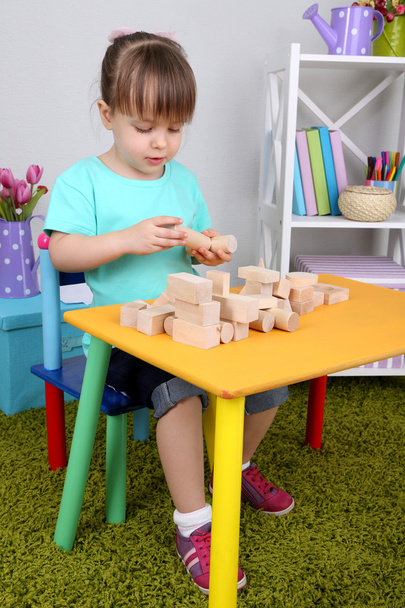 Little girl plays with construction blocks sitting at table in room - 写真・画像