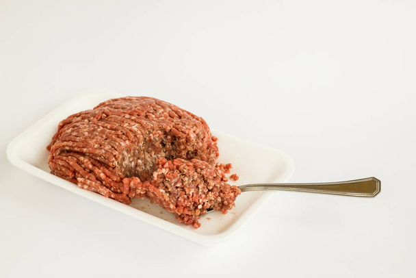 Főzetlen darált marhahús, fehér csomagolásban, kanállal és másolóhellyel. - Fotó, kép