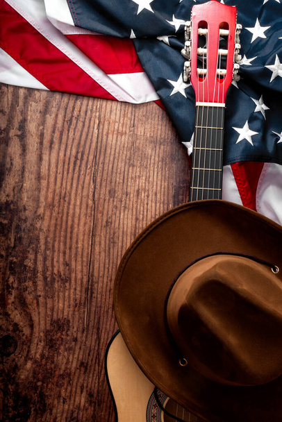 Amerikan kültürü, çiftlik ve country müzik konsepti temalı kovboy şapkası, Amerikan bayrağı ve akustik gitarı olan eski bir salonun ahşap arka planında yaşıyor. - Fotoğraf, Görsel
