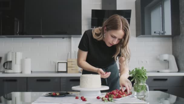 Chef profissional está cozinhando bolo. Jovem dona de casa atraente usa espátula de metal alinha creme branco no bolo de chocolate
 - Filmagem, Vídeo