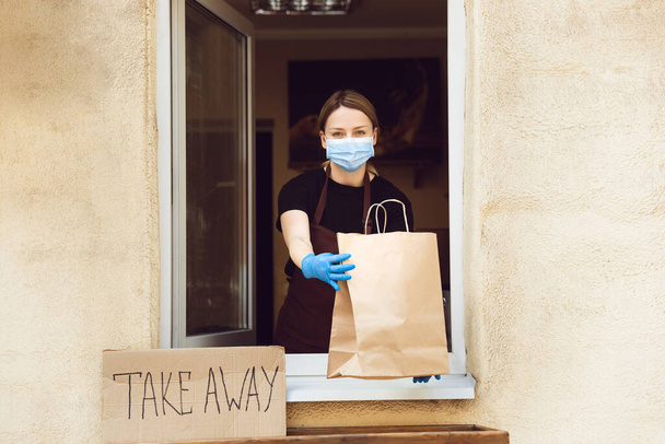 Woman preparing drinks and meals, wearing protective face mask and gloves. Contactless delivery service during quarantine coronavirus pandemic. Take away only concept. - Foto, Bild