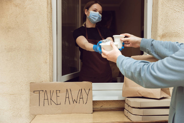 Woman preparing drinks and meals, wearing protective face mask and gloves. Contactless delivery service during quarantine coronavirus pandemic. Take away only concept. - Fotoğraf, Görsel