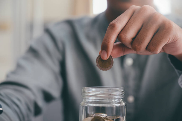 Κοντινό πλάνο αρσενικό χέρι κρατώντας κέρματα βάζοντας σε γυαλί. Εξοικονόμηση χρημάτων για τη λογιστική έννοια. - Φωτογραφία, εικόνα