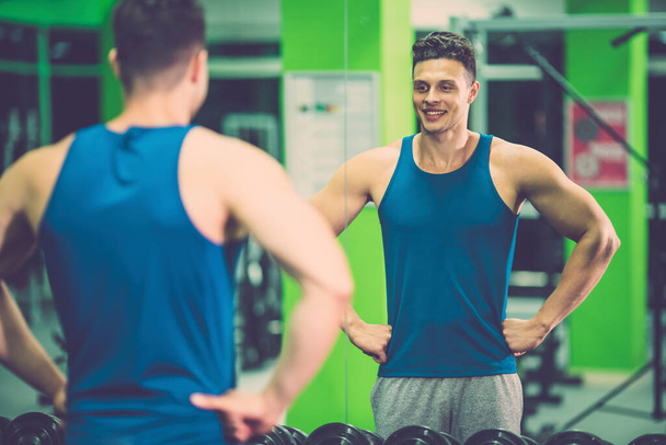 O desportista feliz olha no espelho no clube de fitness
 - Foto, Imagem