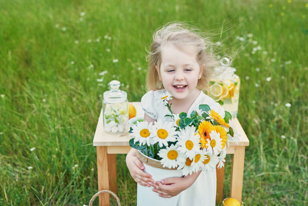 Kind meisje met limonade. Limonade en madeliefjes bloemen op tafel. Gezellige ochtend. Voorjaars- en zomerseizoenskaart. Gezond eten en drinken. Zomervakantie. Een picknick buiten. Moederdagskaart - Foto, afbeelding