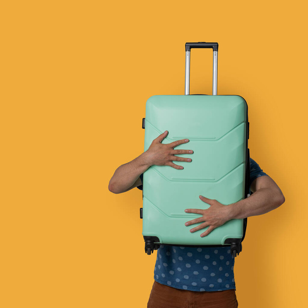 Plastic light green suitcase in male hands. Caucasian man holds a suitcase in front of himself while posing in studio on a colored background. Travel concept - Foto, Imagen