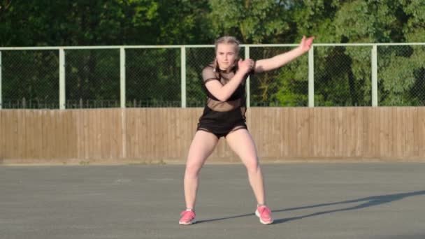 Videó egy aktív fiatal nőről, aki utcai modern táncot táncol, és a színpadon tekergőzik a rivaldafény előtt. Szextánc. Ifjúsági szubkultúra. Lassú mozgás. - Felvétel, videó