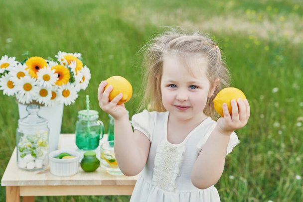 Lapsityttö limonadilla. Limonadia ja päivänkakkaroita pöydällä. Mukava aamu. Kevään ja kesän kortti. Terveellistä ruokaa ja juomaa. Kesälomat. Ulkona piknikillä. Äitienpäiväkortti - Valokuva, kuva