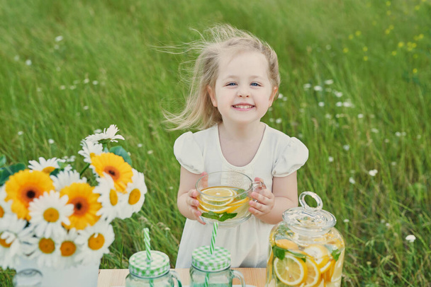Kind meisje met limonade. Limonade en madeliefjes bloemen op tafel. Gezellige ochtend. Voorjaars- en zomerseizoenskaart. Gezond eten en drinken. Zomervakantie. Een picknick buiten. Moederdagskaart - Foto, afbeelding