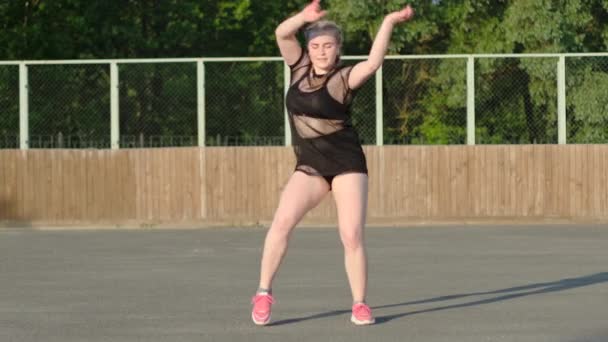 Videó egy aktív fiatal nőről, aki utcai modern táncot táncol, és a színpadon tekergőzik a rivaldafény előtt. Szextánc. Ifjúsági szubkultúra. Lassú mozgás. - Felvétel, videó