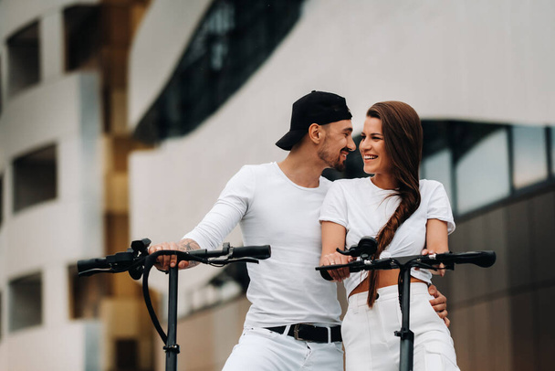 A girl and a guy are walking on electric scooters around the city, a couple in love on scooters - Zdjęcie, obraz