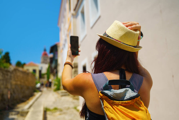 幸せな女性旅行者は歩いていて、ギリシャのロードス島、ドデカネス島、ギリシャの電話で自撮り写真を撮っています - 写真・画像