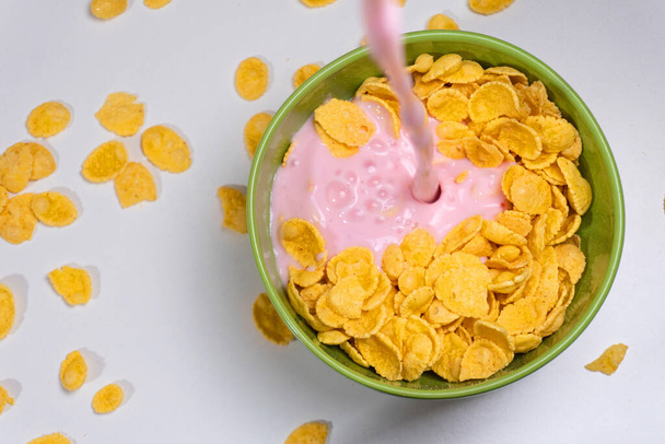 Verter yogur desde la vista superior sobre los copos de maíz
 - Foto, imagen