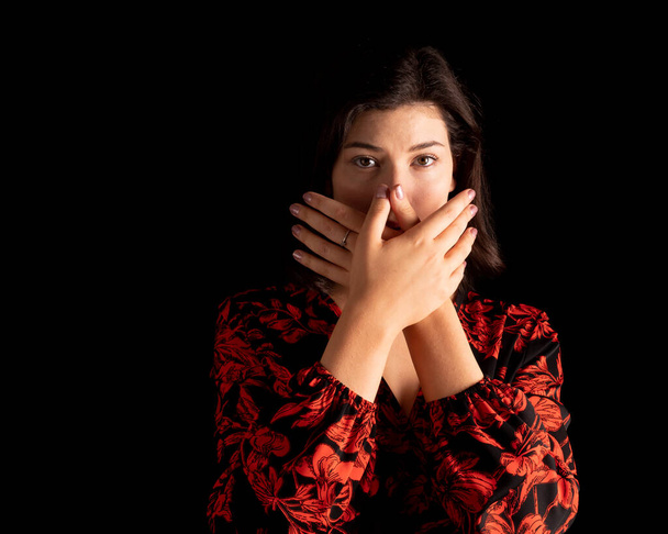 woman with hands over her mouth, black background. Gender violence concept - Foto, afbeelding