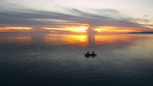 Luchtfoto van drone glijden over zee oppervlak tijdens gouden uur middag zonsondergang. Prachtige filmische zonneschijn op vlakke waterkolom met silhouet van vissers in de verte. Vrij heldere lucht. - Video